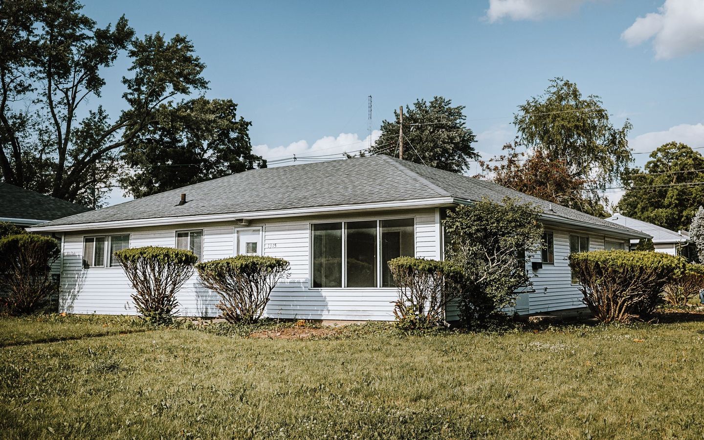 A white house with a gray roof is sitting in the middle of a lush green field.