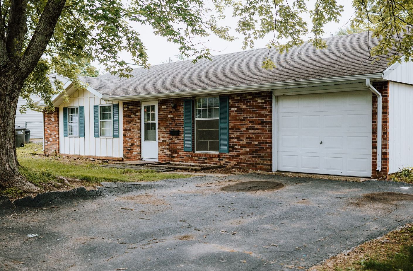 A brick house with a white garage door and blue shutters.