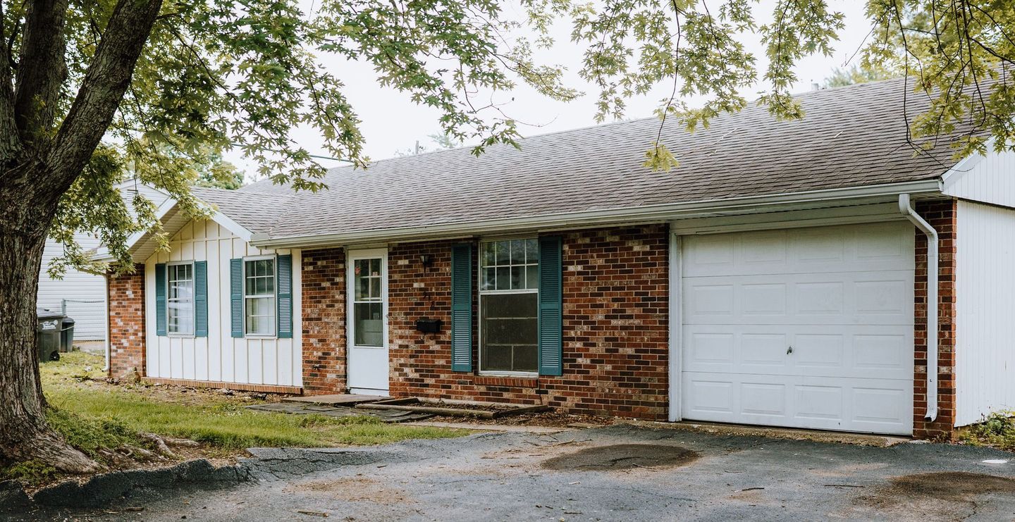A brick house with a white garage door and blue shutters.