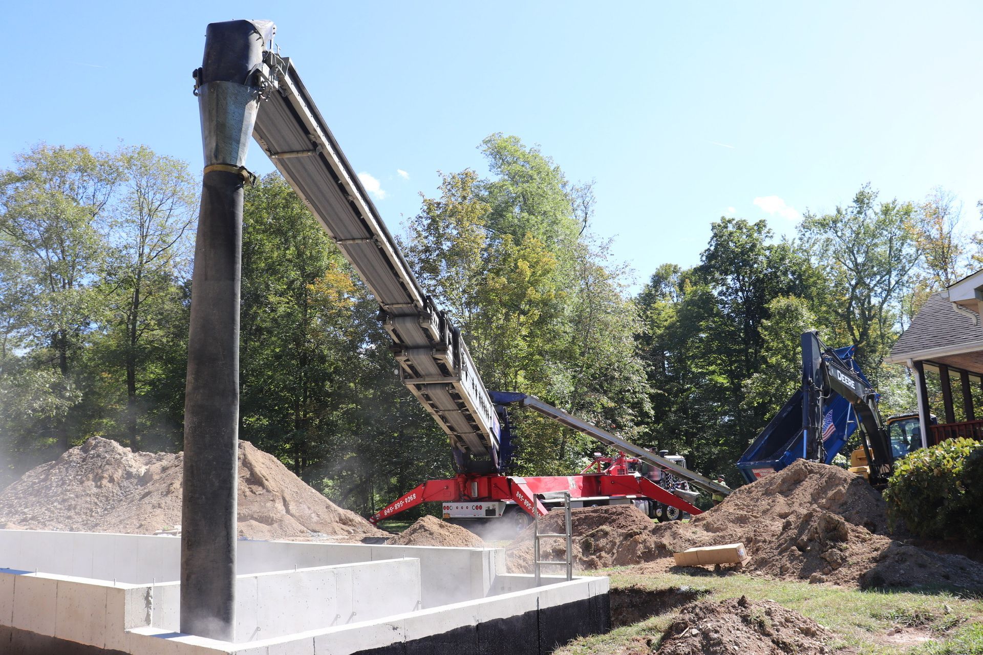 A red crane is loading dirt into a concrete foundation.