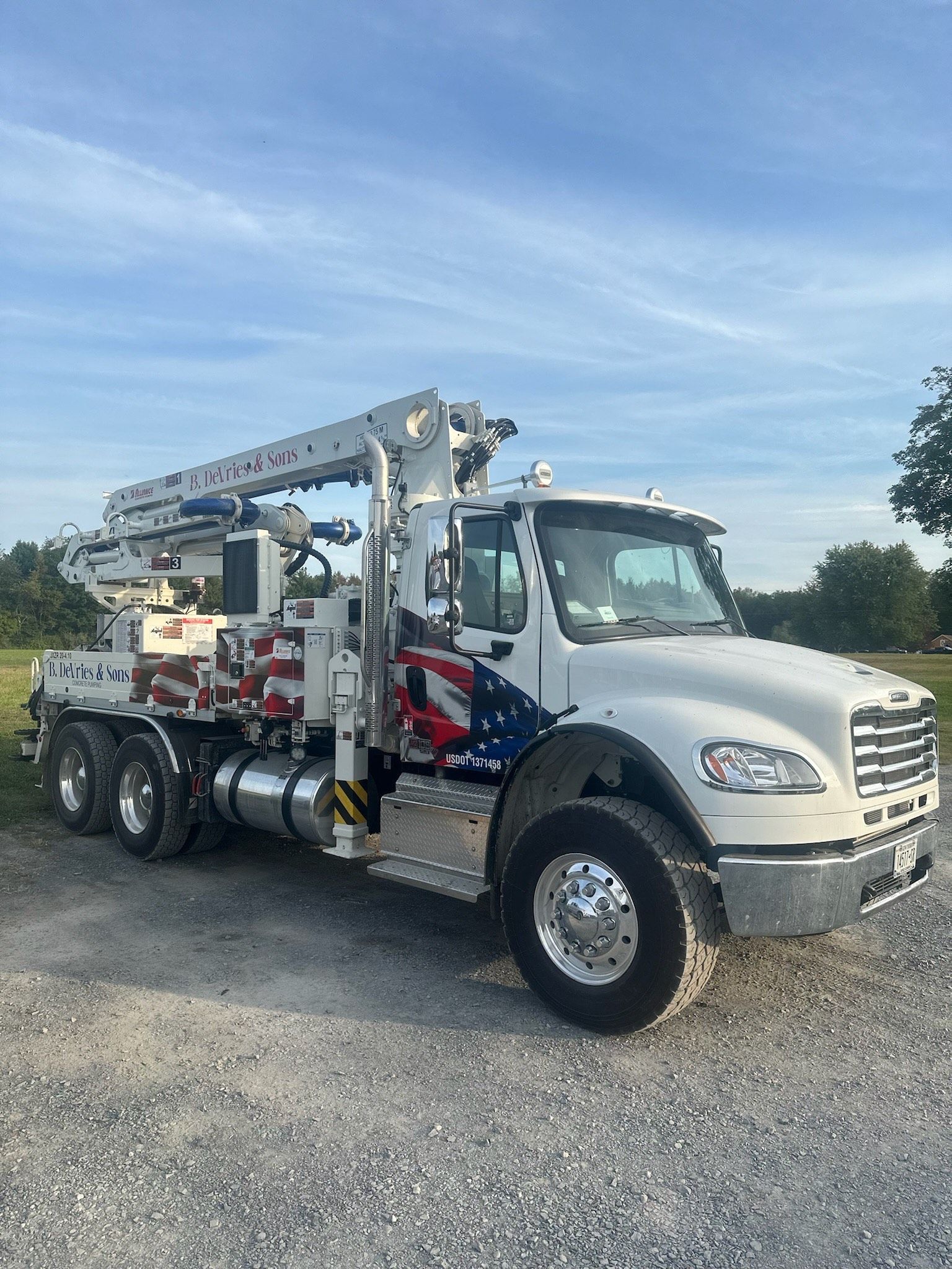 A white truck with an american flag painted on the side is parked in a gravel lot.