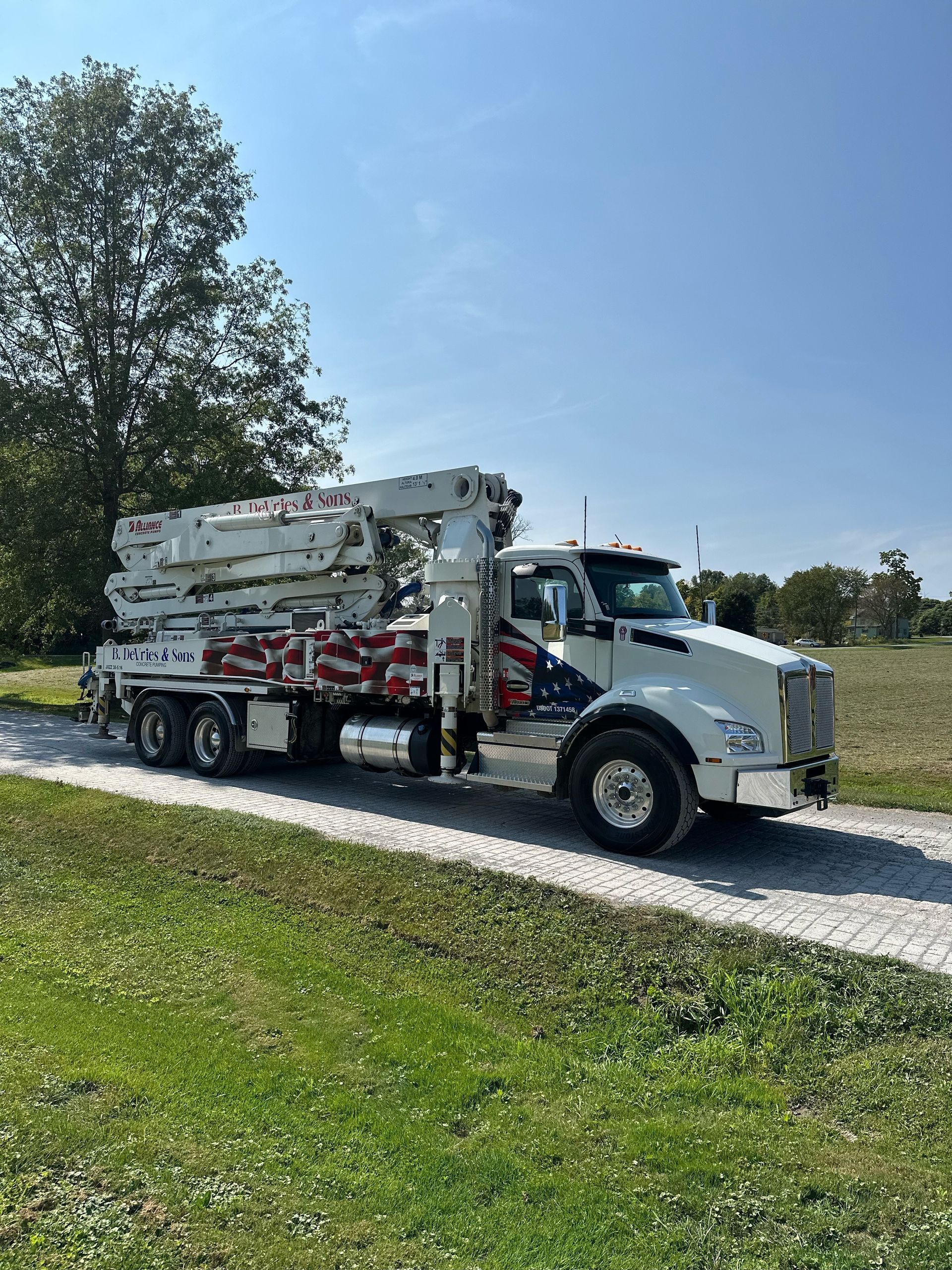 A concrete pump truck is parked on the side of a dirt road.