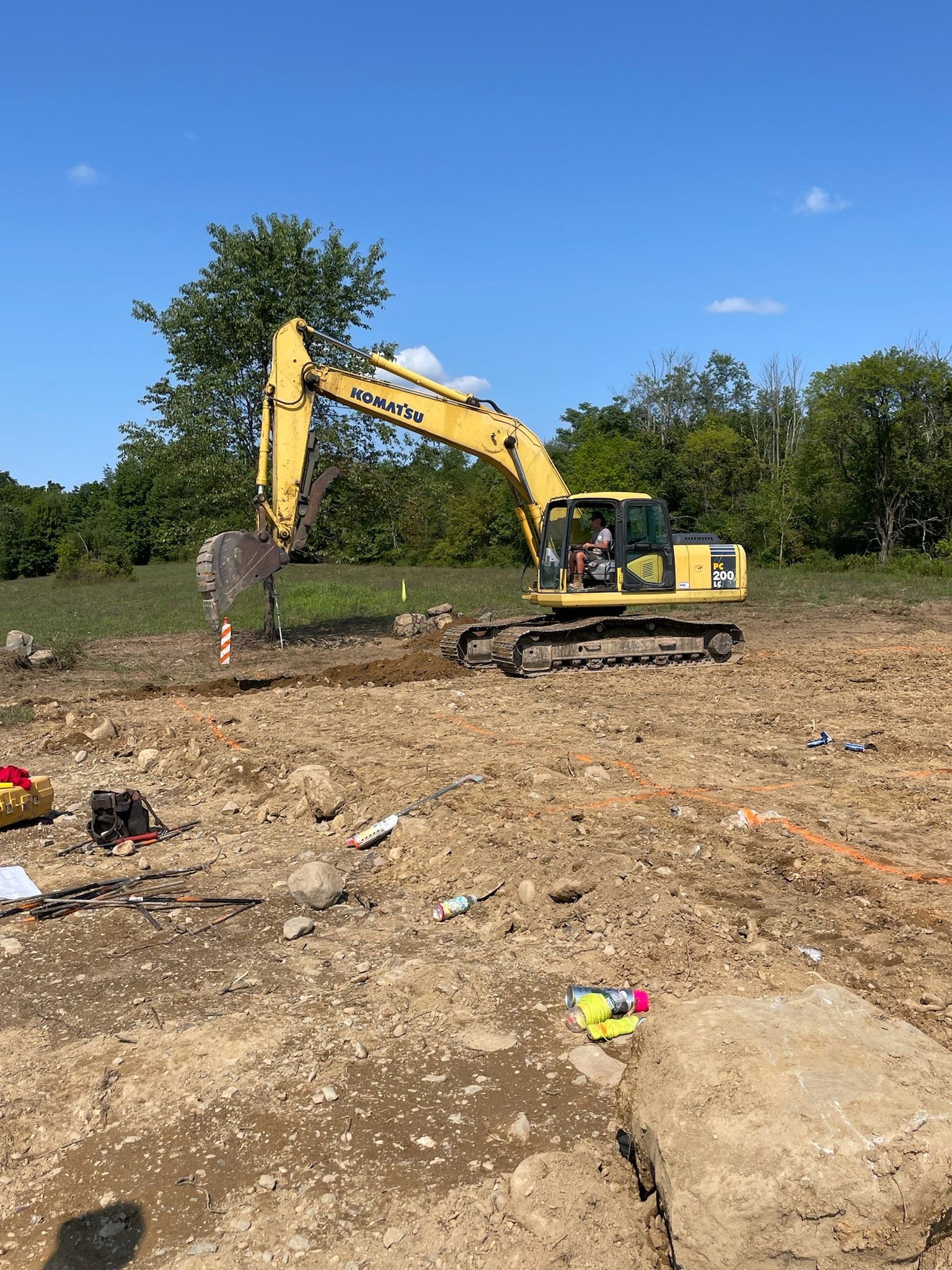 A yellow excavator is digging a hole in a dirt field.