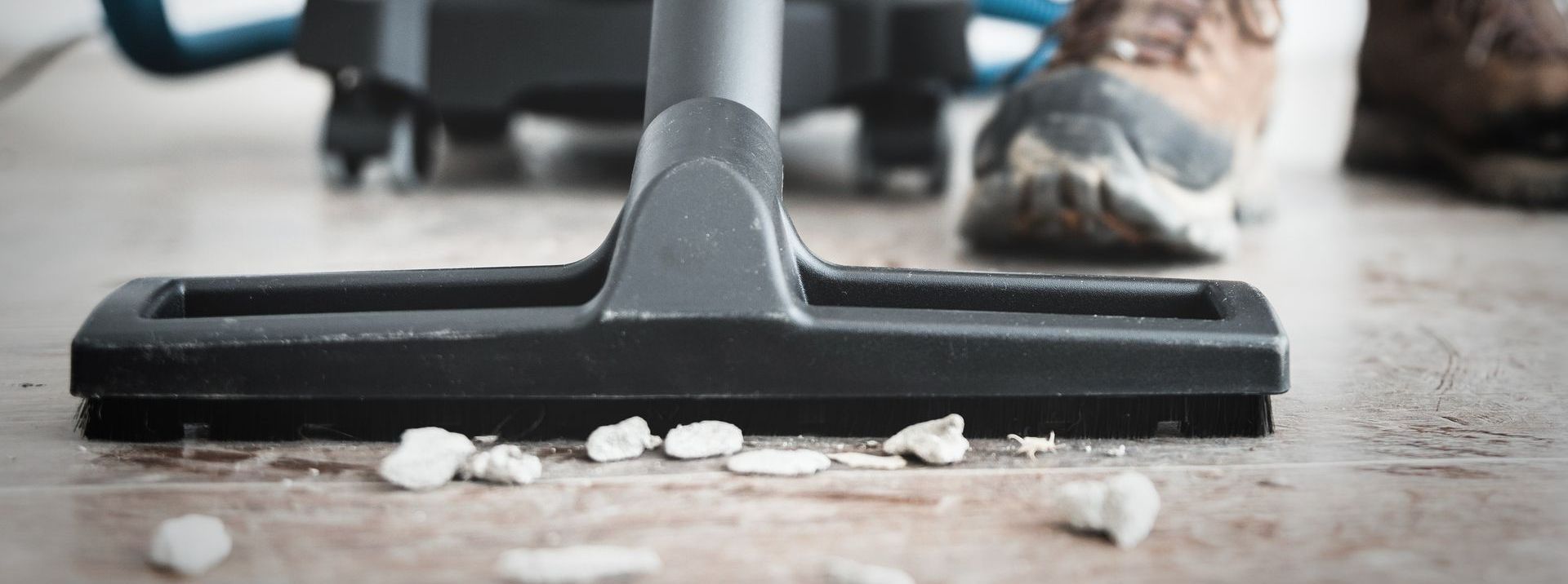 Une tête d'aspirateur nettoie des débris sur un parquet. Une personne est visible.