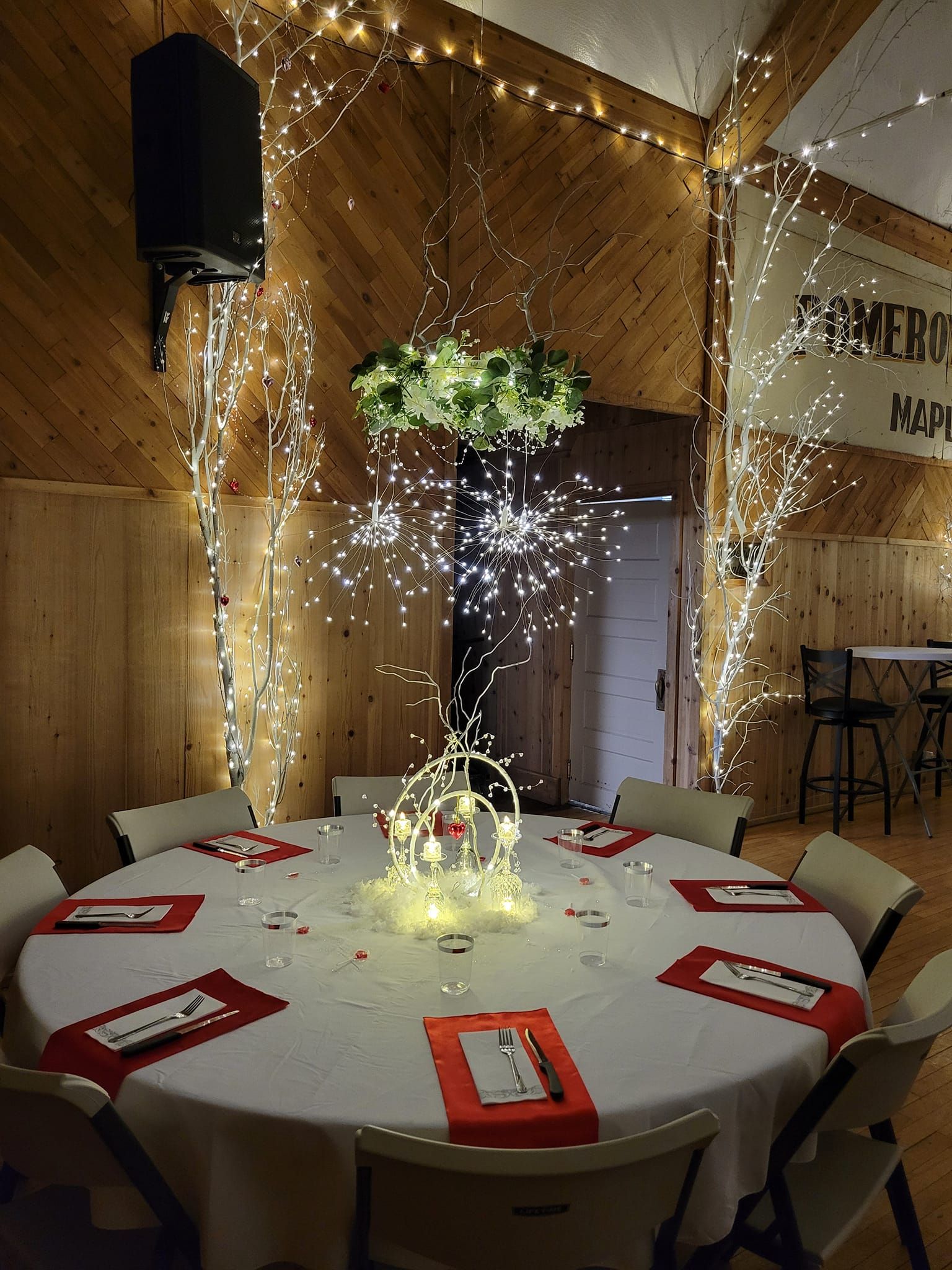 Round table set for an event, decorated with white and red accents, fairy lights in a rustic wood-paneled interior