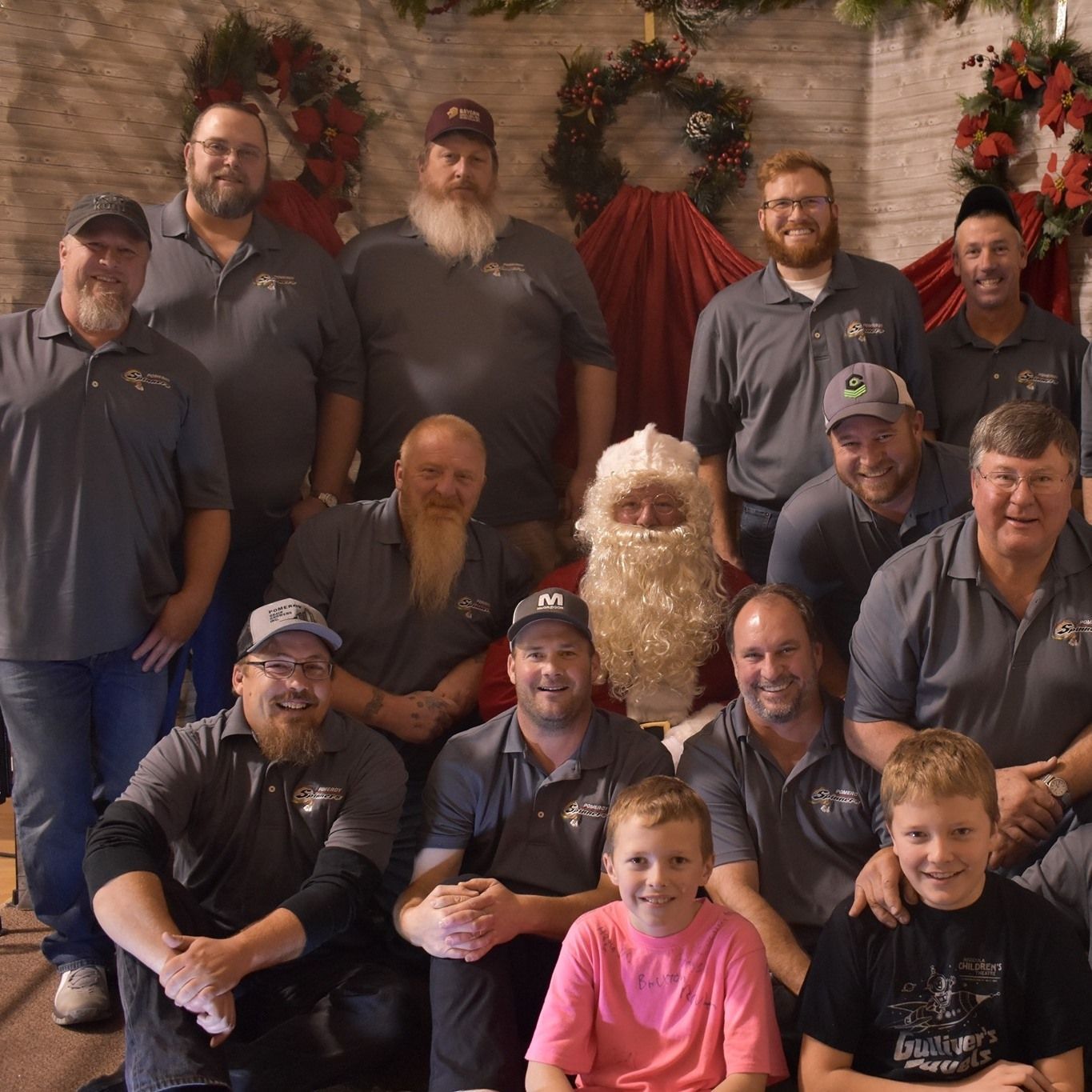 Group of men, Santa Claus, and two kids posing for a photo in front of Christmas decorations