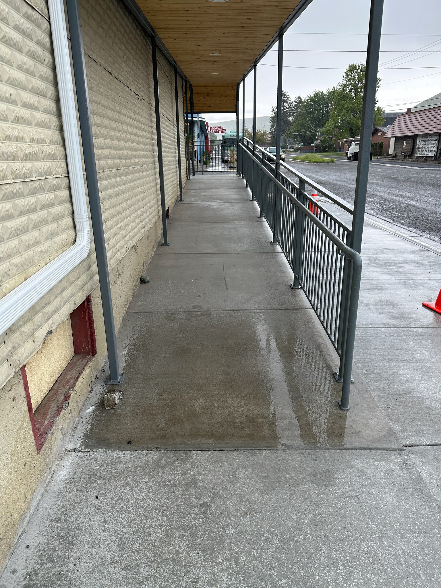Concrete ramp with railings along a building's exterior, leading to a street. Wet pavement.