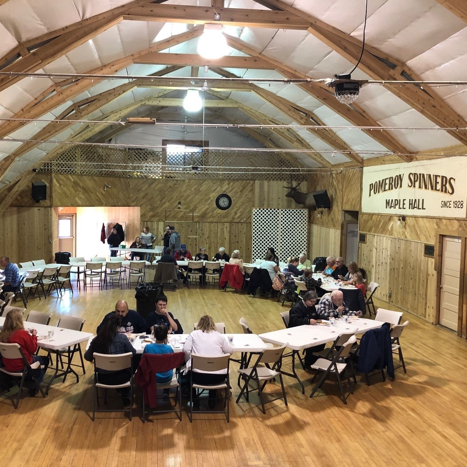 People seated at tables in a large hall with wood paneling and a high ceiling