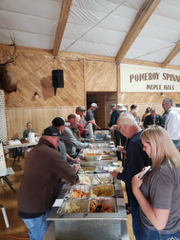 People line up at a buffet in a hall with wood paneling