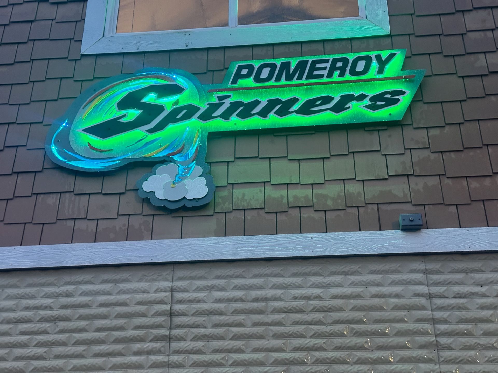 Pomeroy Spinners sign: green neon logo on a brown shingled building.