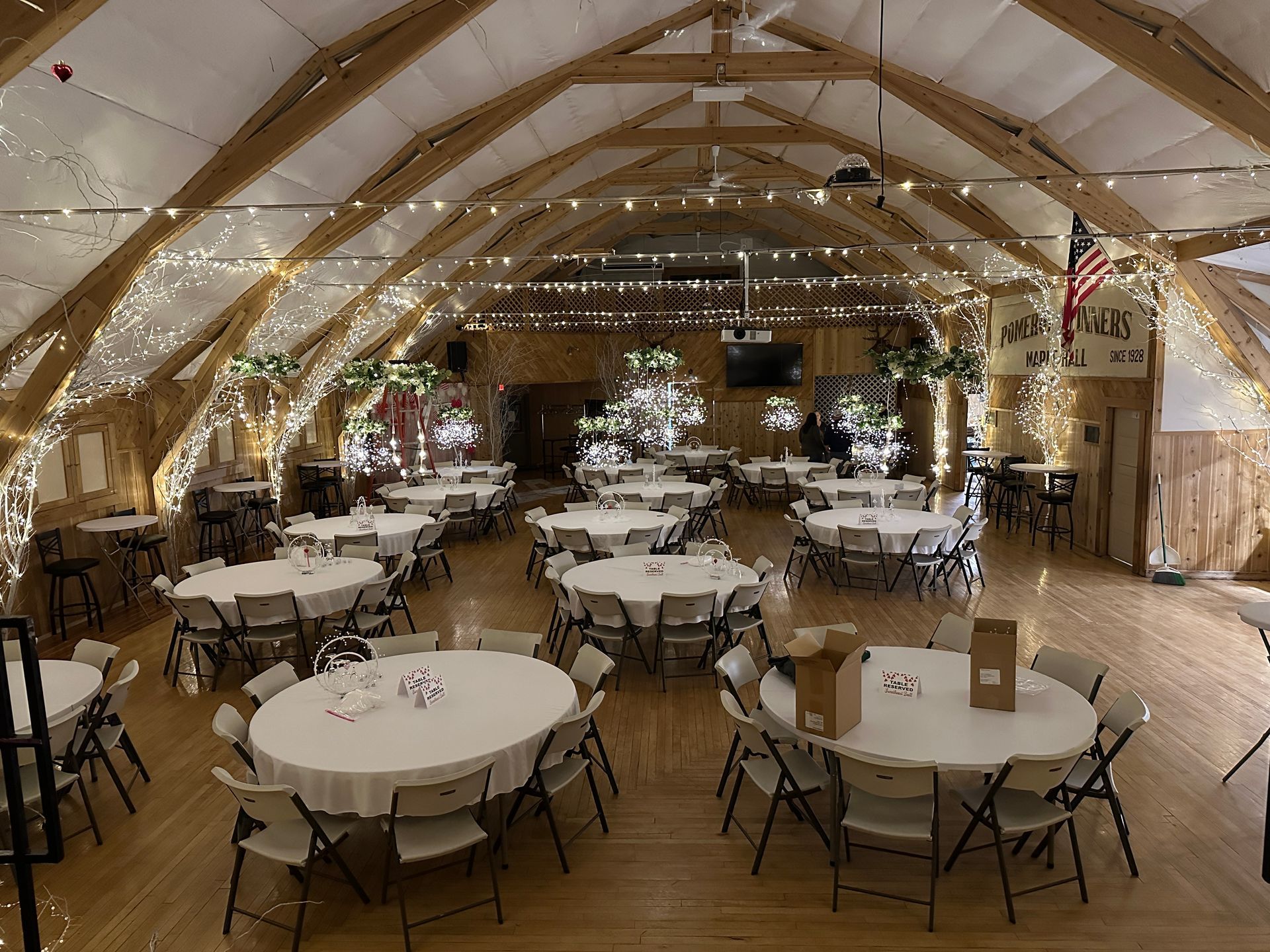 Reception hall decorated for an event, with round tables, chairs, and string lights.