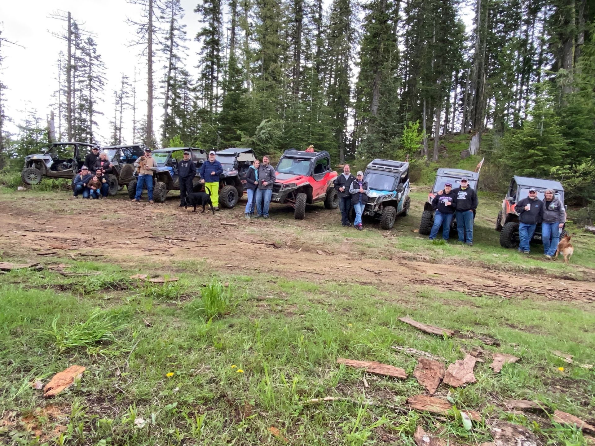 Group of people and ATVs in a muddy clearing in a forest.
