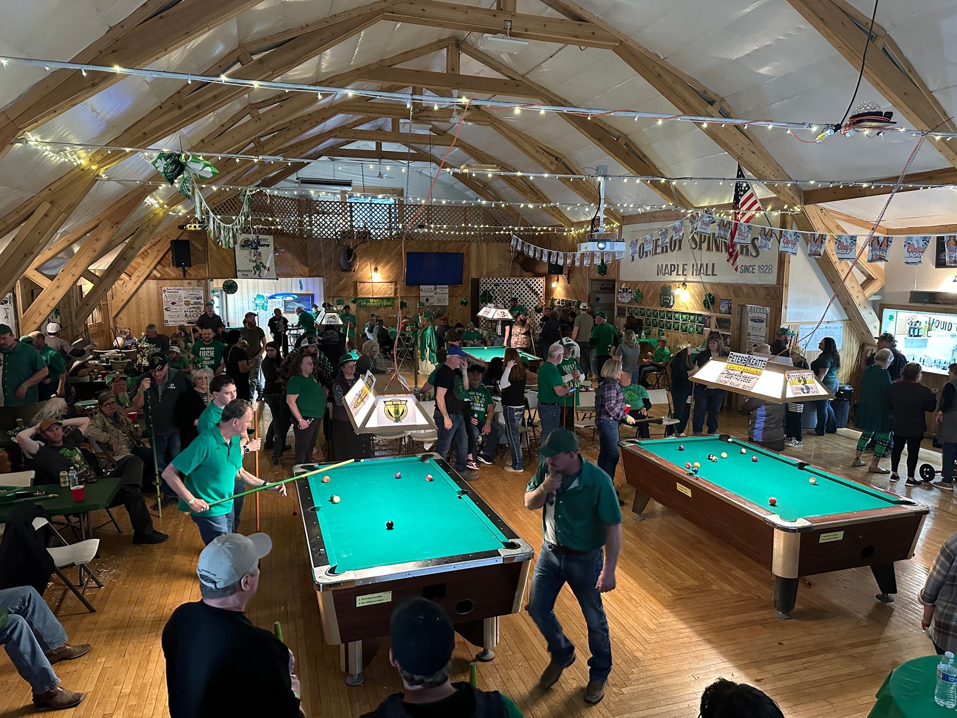 People in green attire play pool in a large, festive hall decorated for an event.
