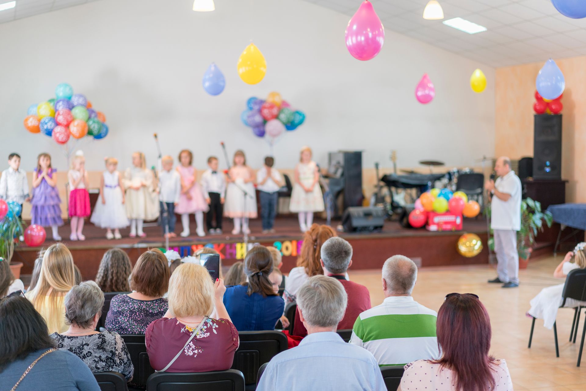 Children in formal wear perform on a stage with balloons