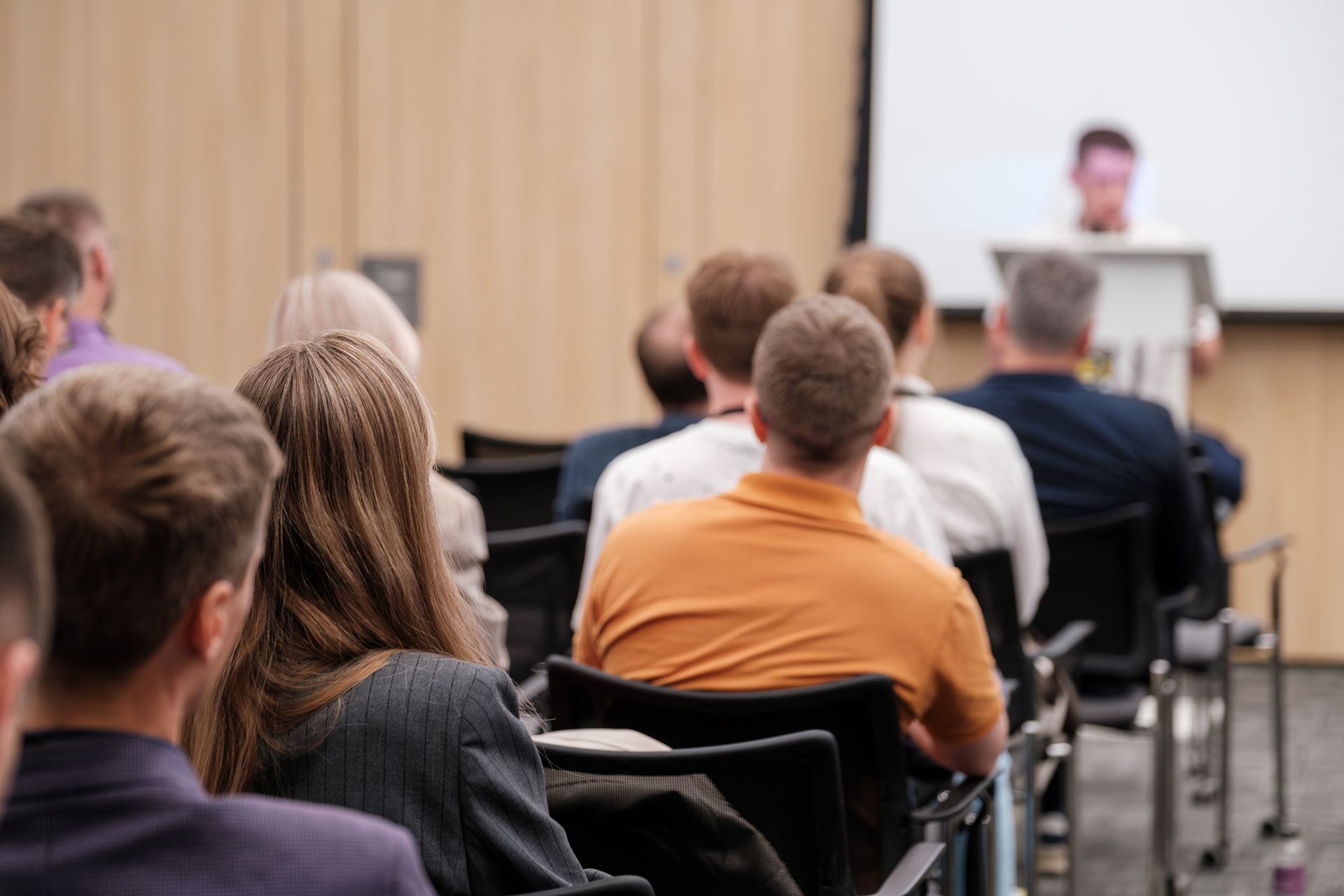 Audience in a conference room listens to a presenter at a podium
