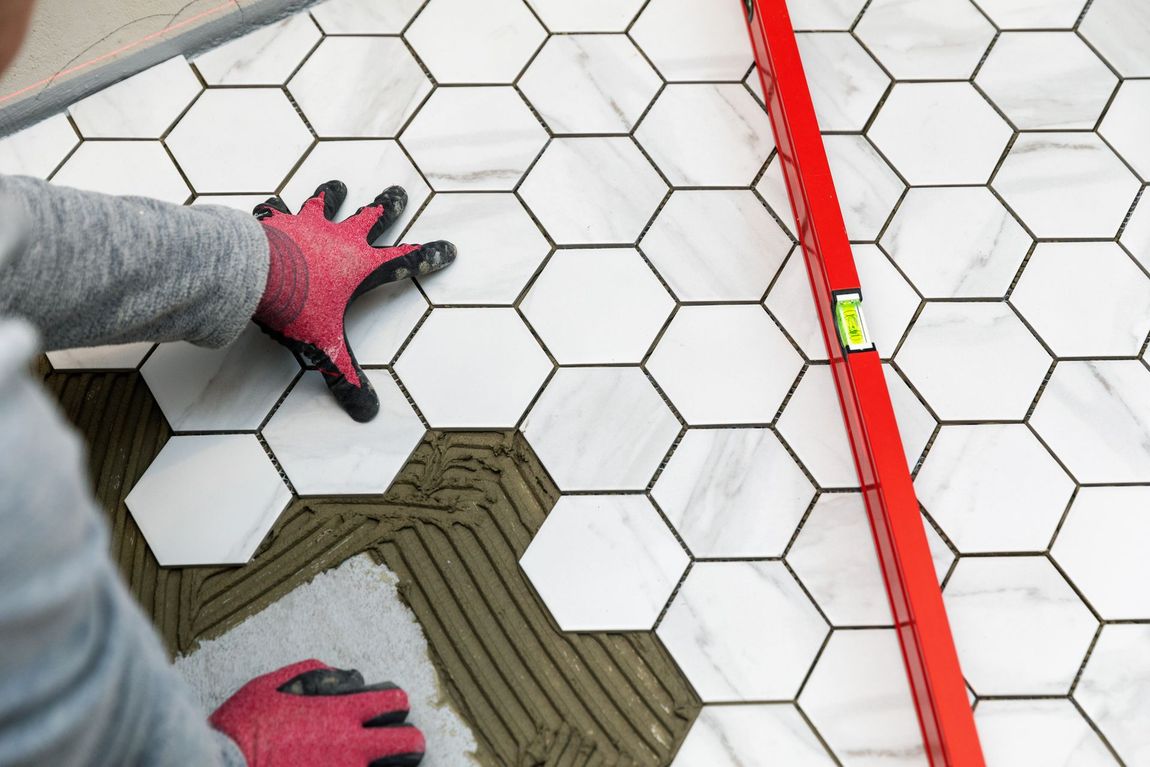 A person is laying tiles on a floor with a level.