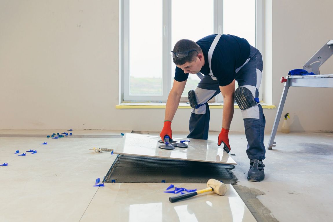 A man is laying a tile floor in a room.