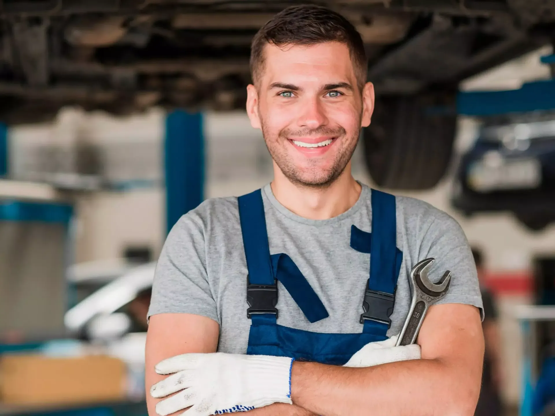 Um homem de macacão segurando uma chave inglesa e sorrindo em uma garagem