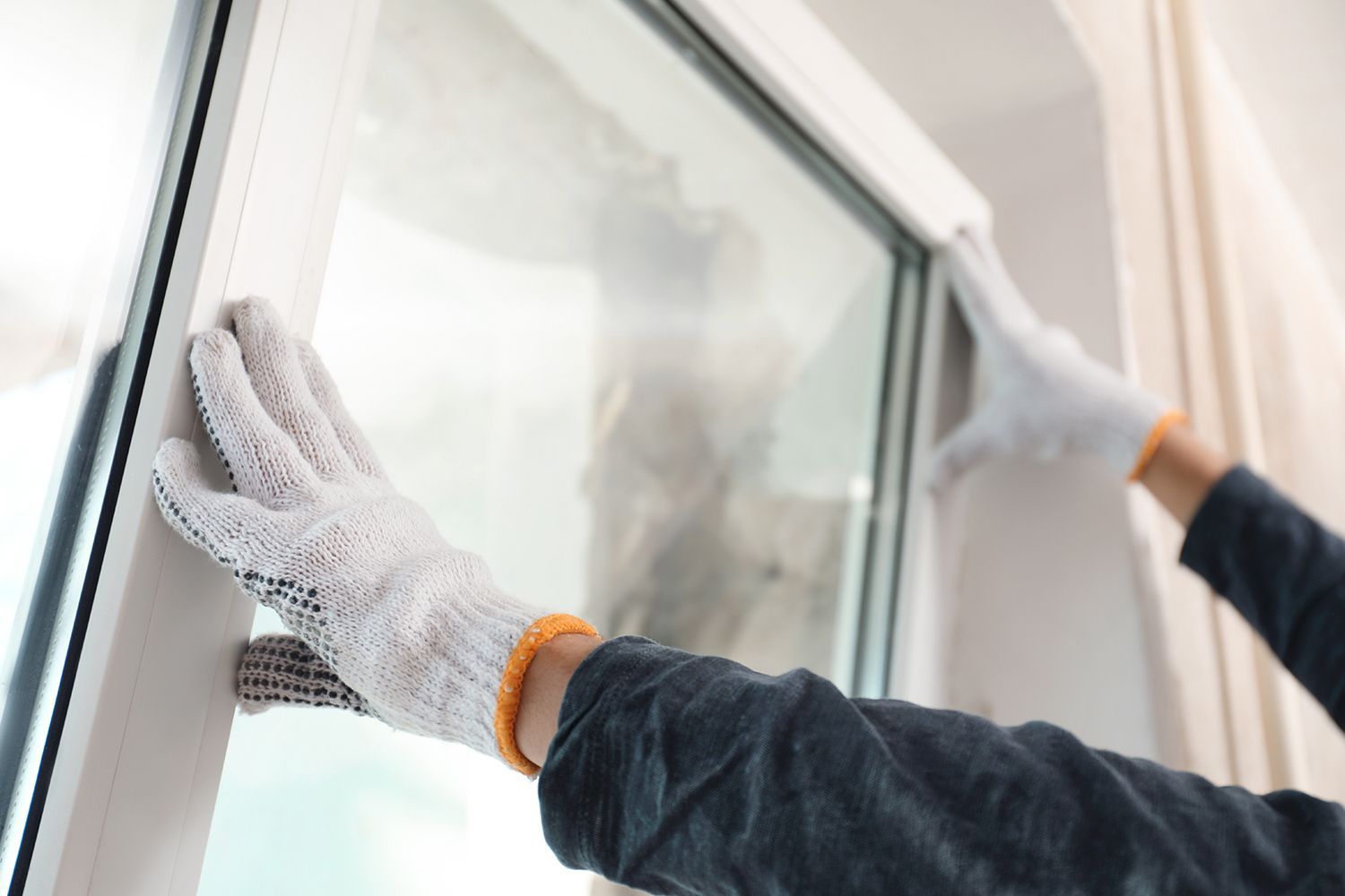 Gloved hands installing or adjusting a window frame from indoors.