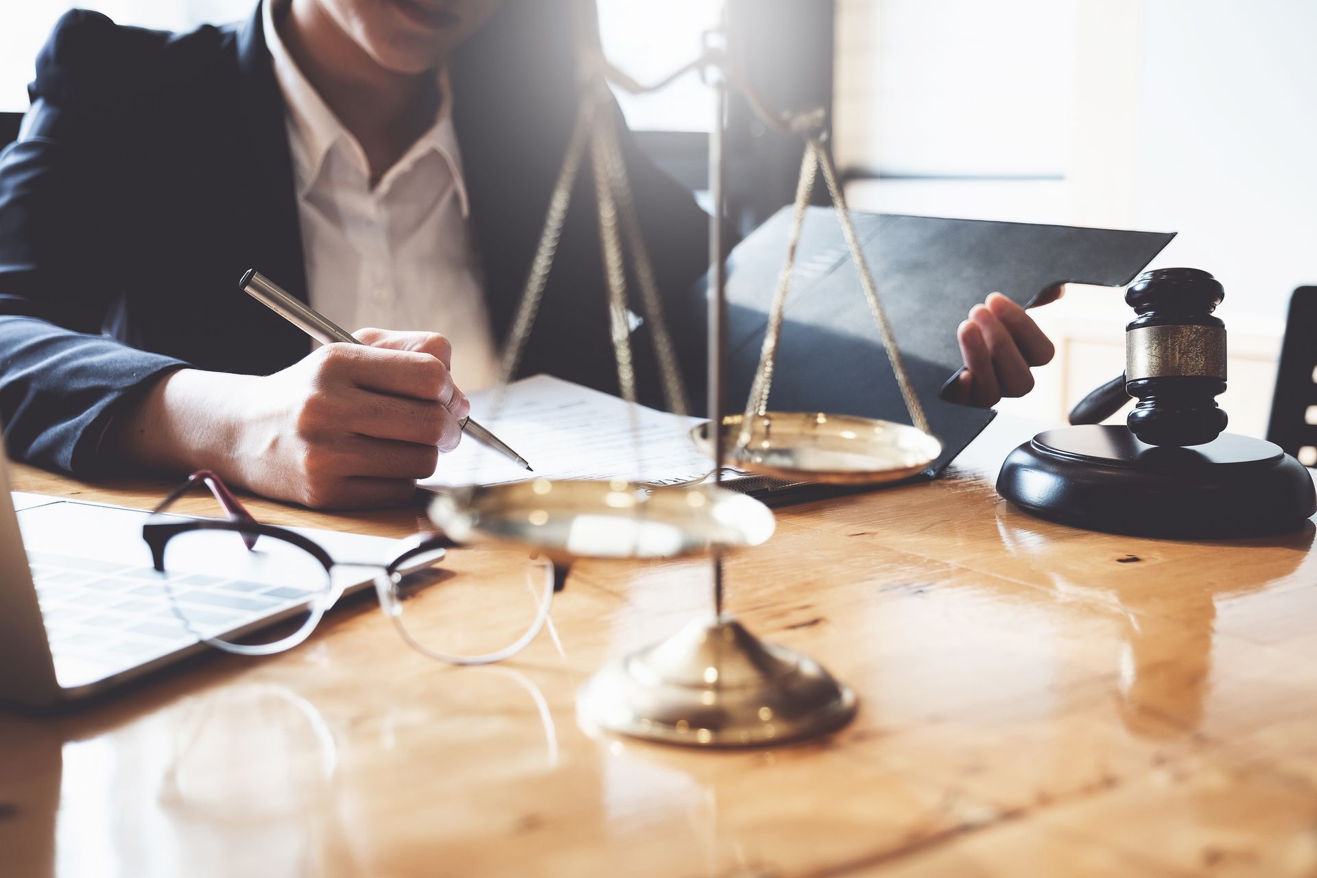 Lawyer signing documents at a desk with scales of justice and a gavel on a wooden table