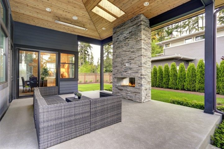 Covered patio with gray wicker seating, stone fireplace, and backyard view
