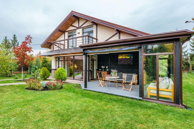 Modern house with a covered patio, outdoor seating, and a green lawn in front.
