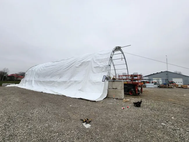 A large white tarp is covering a building in a gravel lot.
