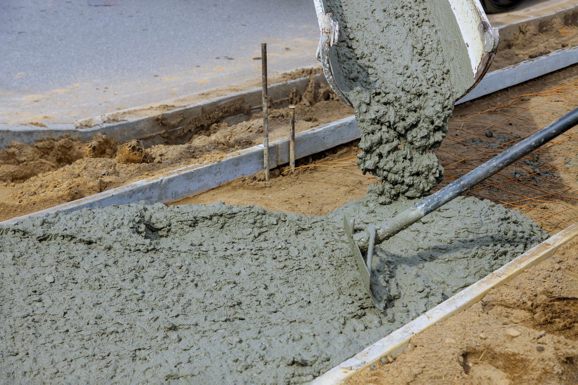 A person is pouring concrete on a sidewalk with a shovel.