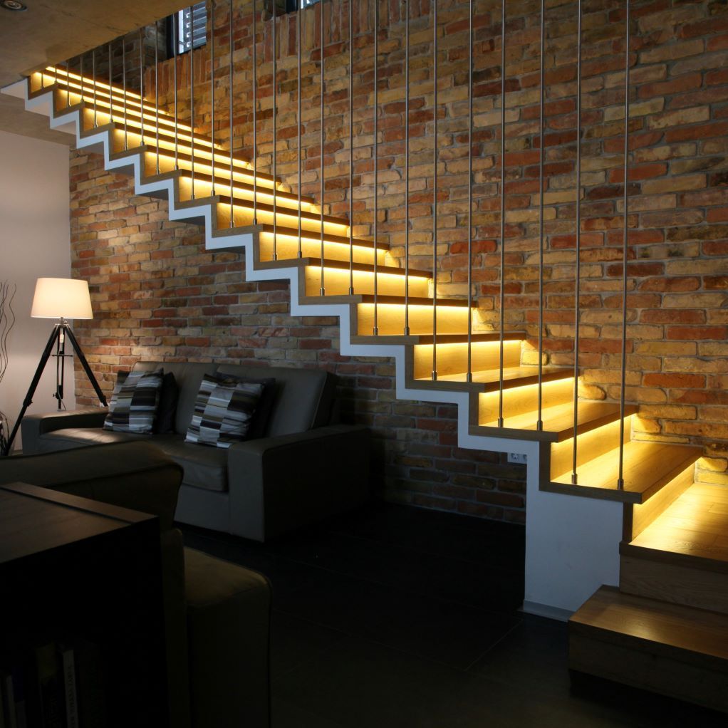 Un escalier est éclairé dans un salon avec un mur de briques