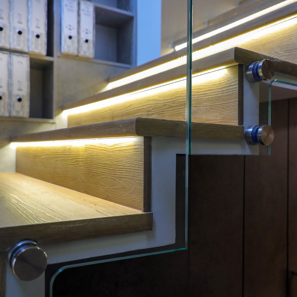 Un escalier en bois avec une rampe en verre et des lumières sur les marches