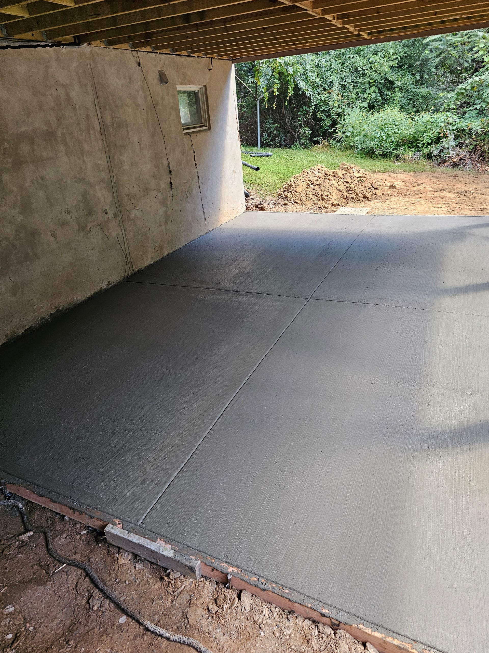 Newly poured concrete slab under a building's overhang; outdoor setting.