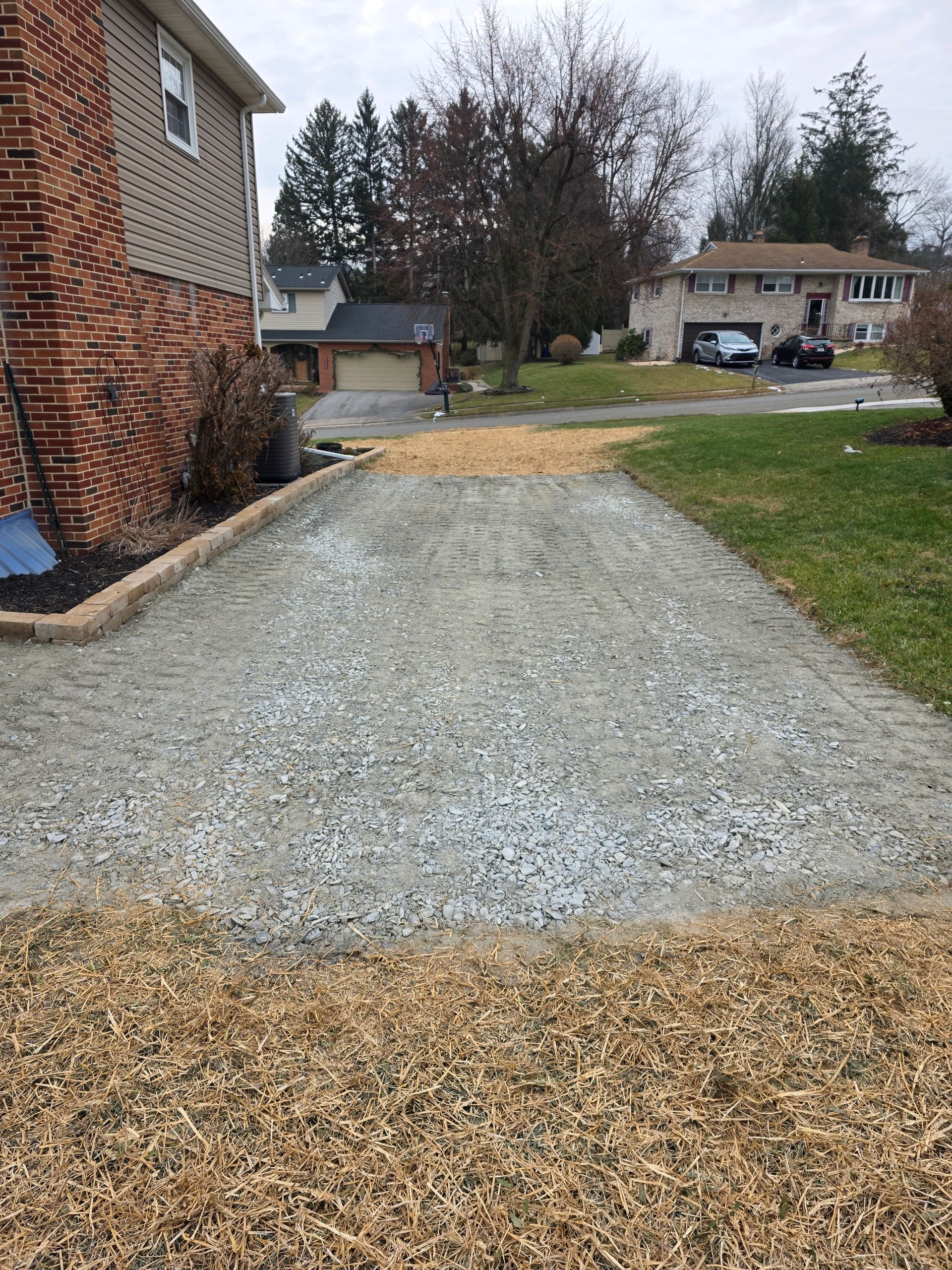 Gravel driveway next to a brick house and grass lawn.