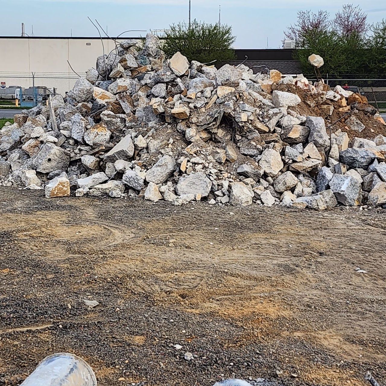 Pile of gray and tan rubble on a gravel lot near a building.