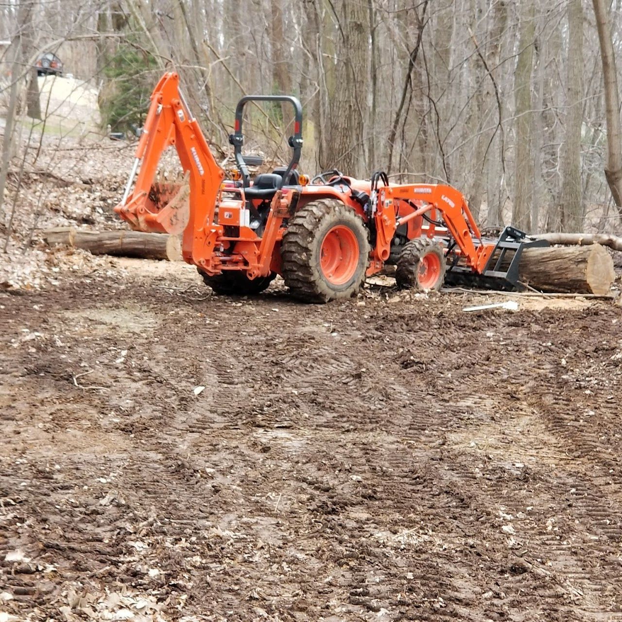 Orange tractor in muddy forest setting; front loader lifting a log.