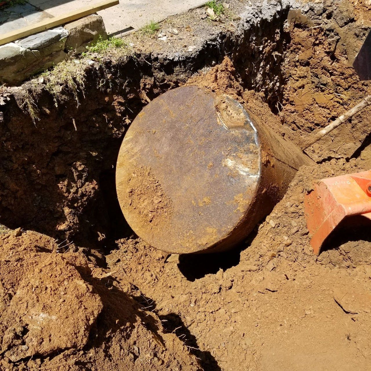 Rusty, cylindrical underground fuel tank exposed in a dirt excavation.