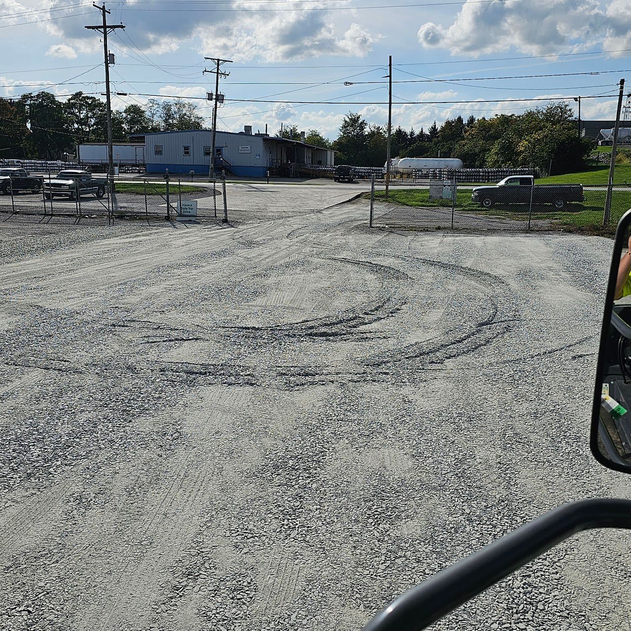 Gravel parking lot with tire tracks, power poles, and a glimpse of a building on a cloudy day.