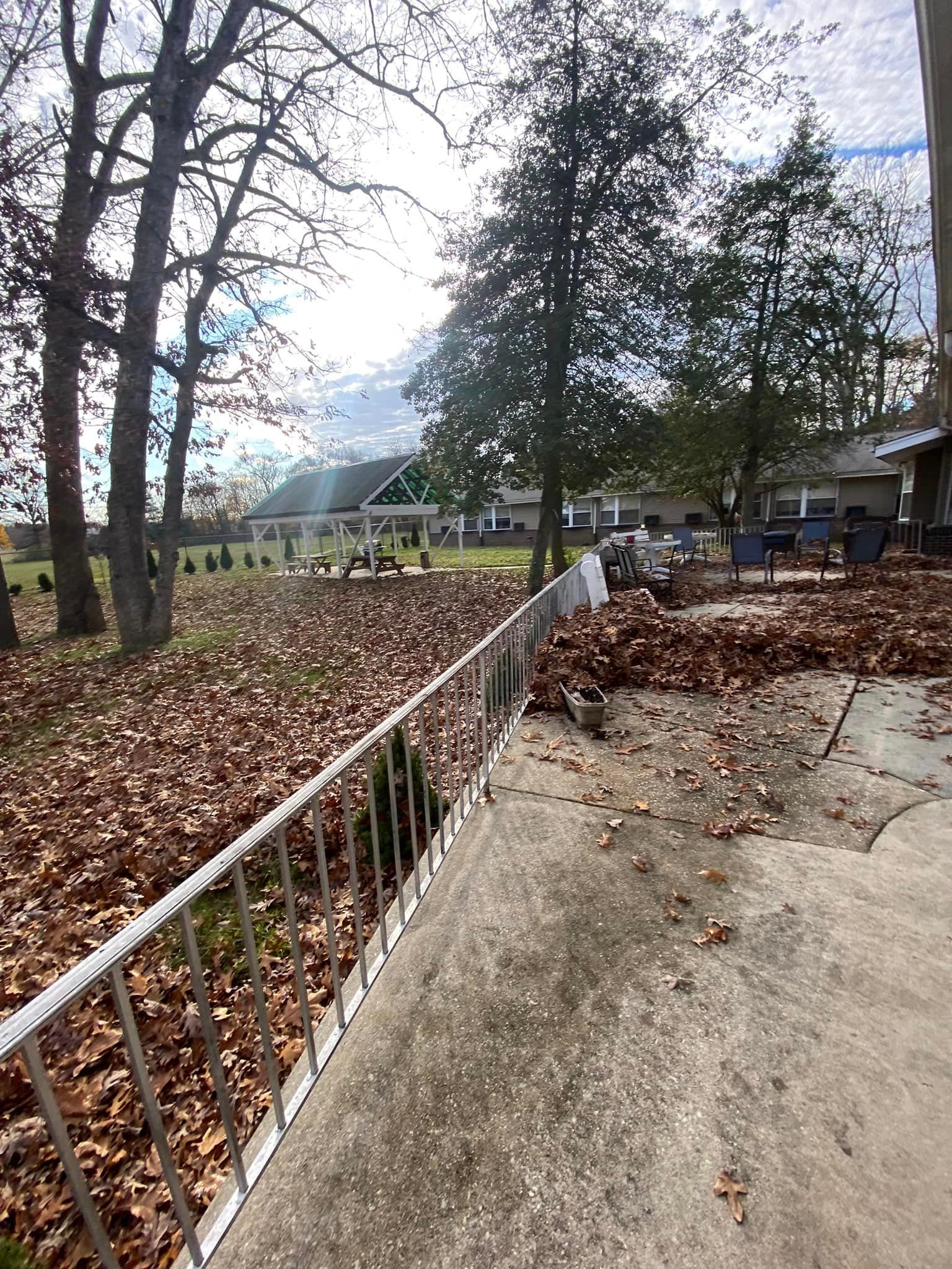 Patio with fall leaves, metal railing, trees, and buildings in the background