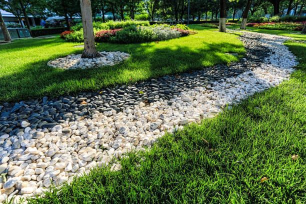 Newly built french drain bordered by green grass, in a sunny garden