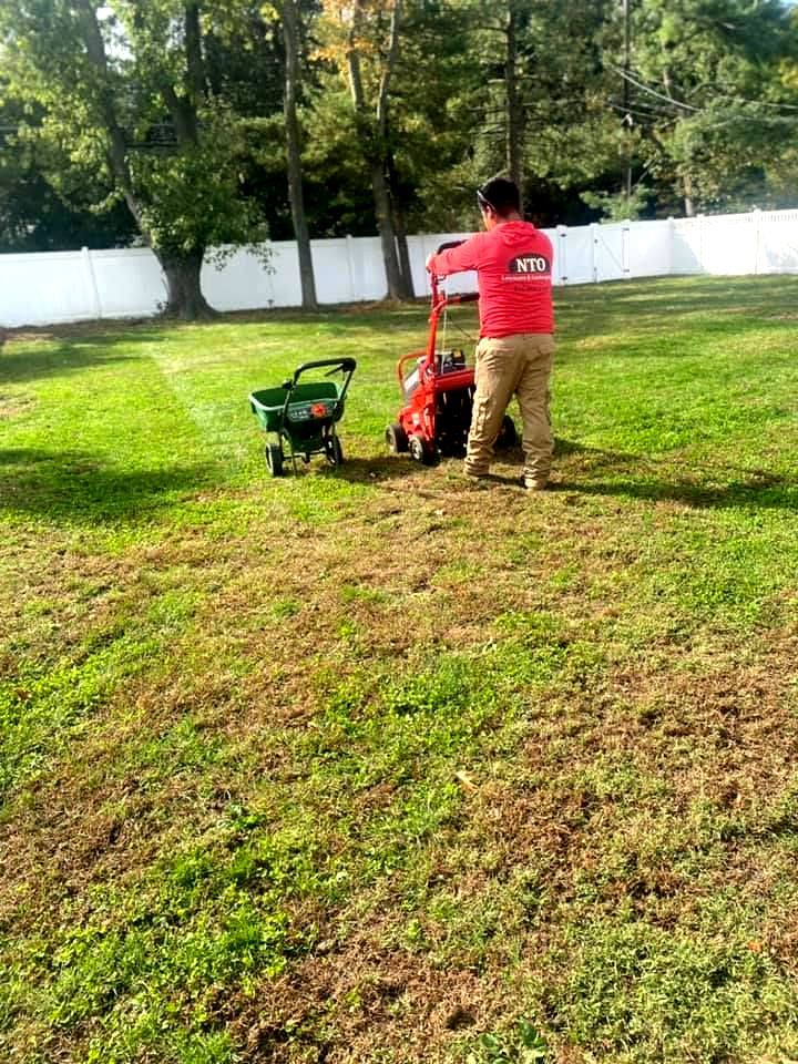 A man is mowing a lawn with a lawn mower and a wheelbarrow.