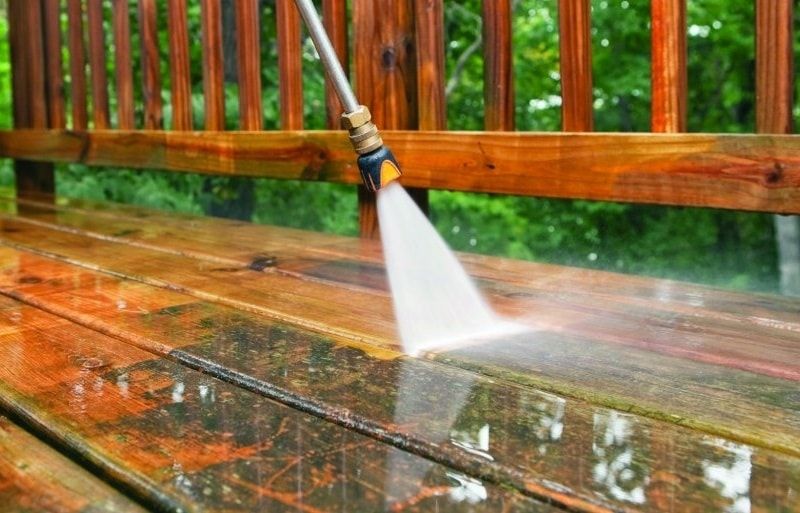 A person is using a high pressure washer to clean a wooden deck.