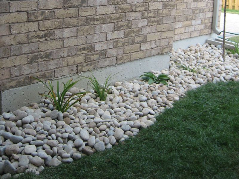 A brick wall is behind a bed of rocks and grass