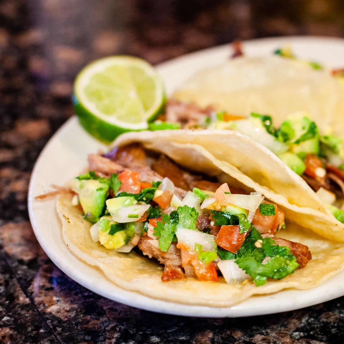 Tacos on a white plate with lime and pico de gallo.