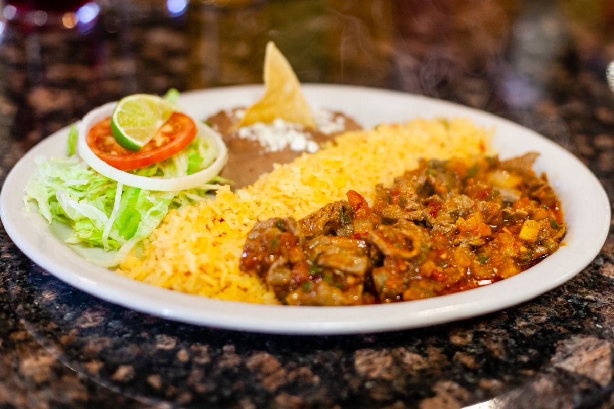 Plate of Mexican food: rice, beans, meat, lettuce, tomato, onion, and lime.