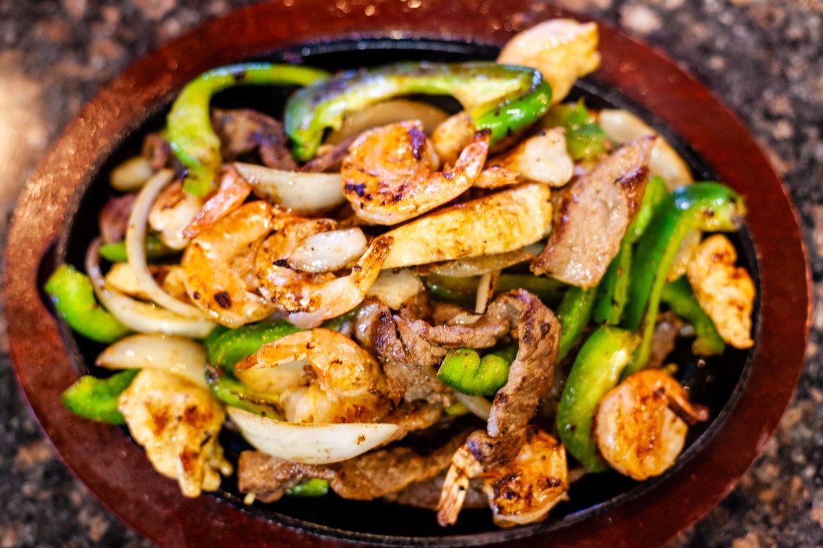Sizzling fajita platter with shrimp, steak, onions, and peppers.