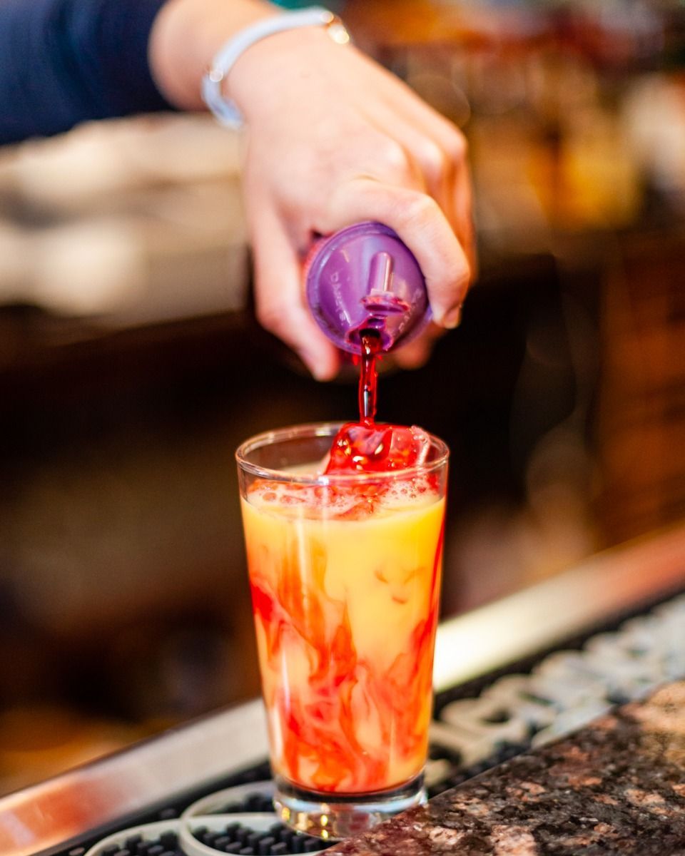 Bartender pouring purple liquid into a layered cocktail with ice.