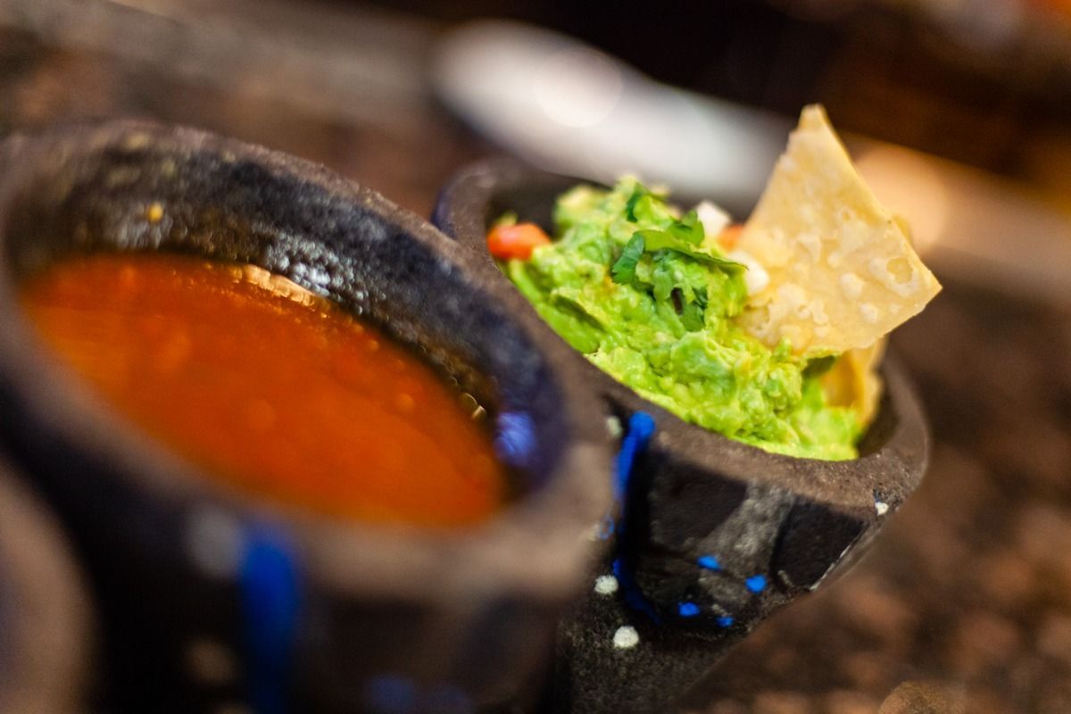 Guacamole and salsa in stone bowls, with a tortilla chip.
