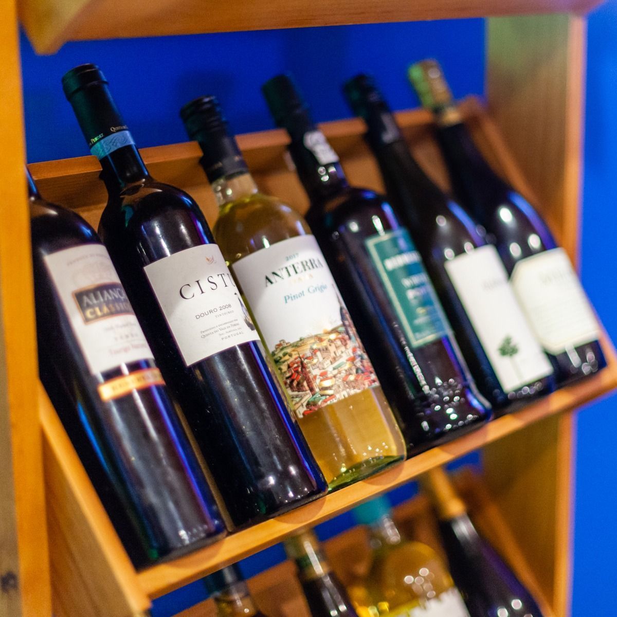 Wine bottles on wooden shelves, angled display. Various labels, dark glass. Blue wall background.