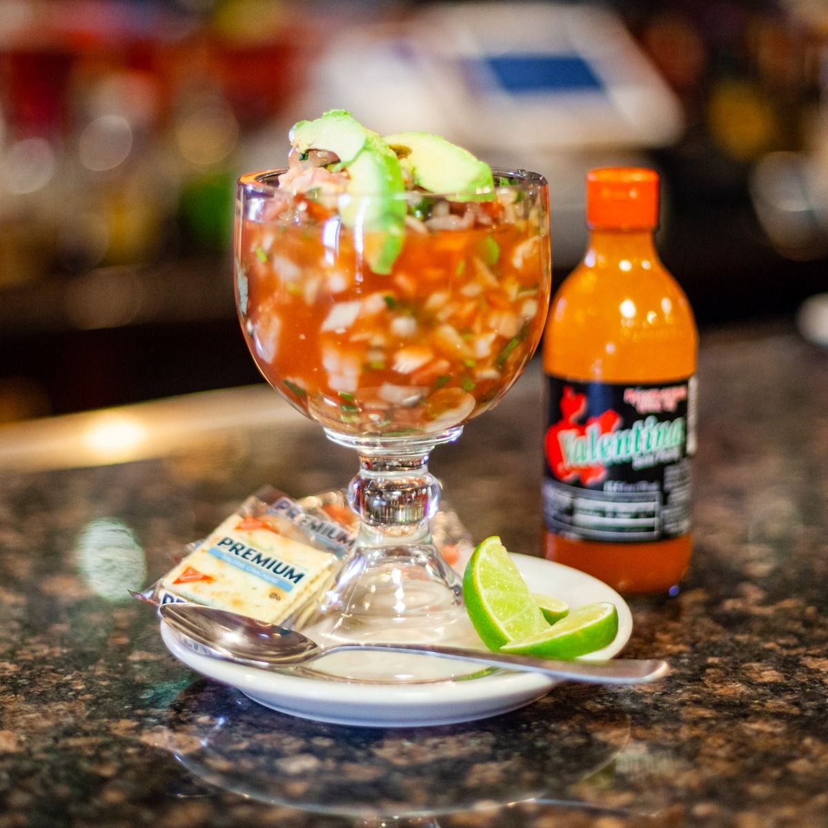 Ceviche in a glass, with crackers, lime, and hot sauce on a plate.