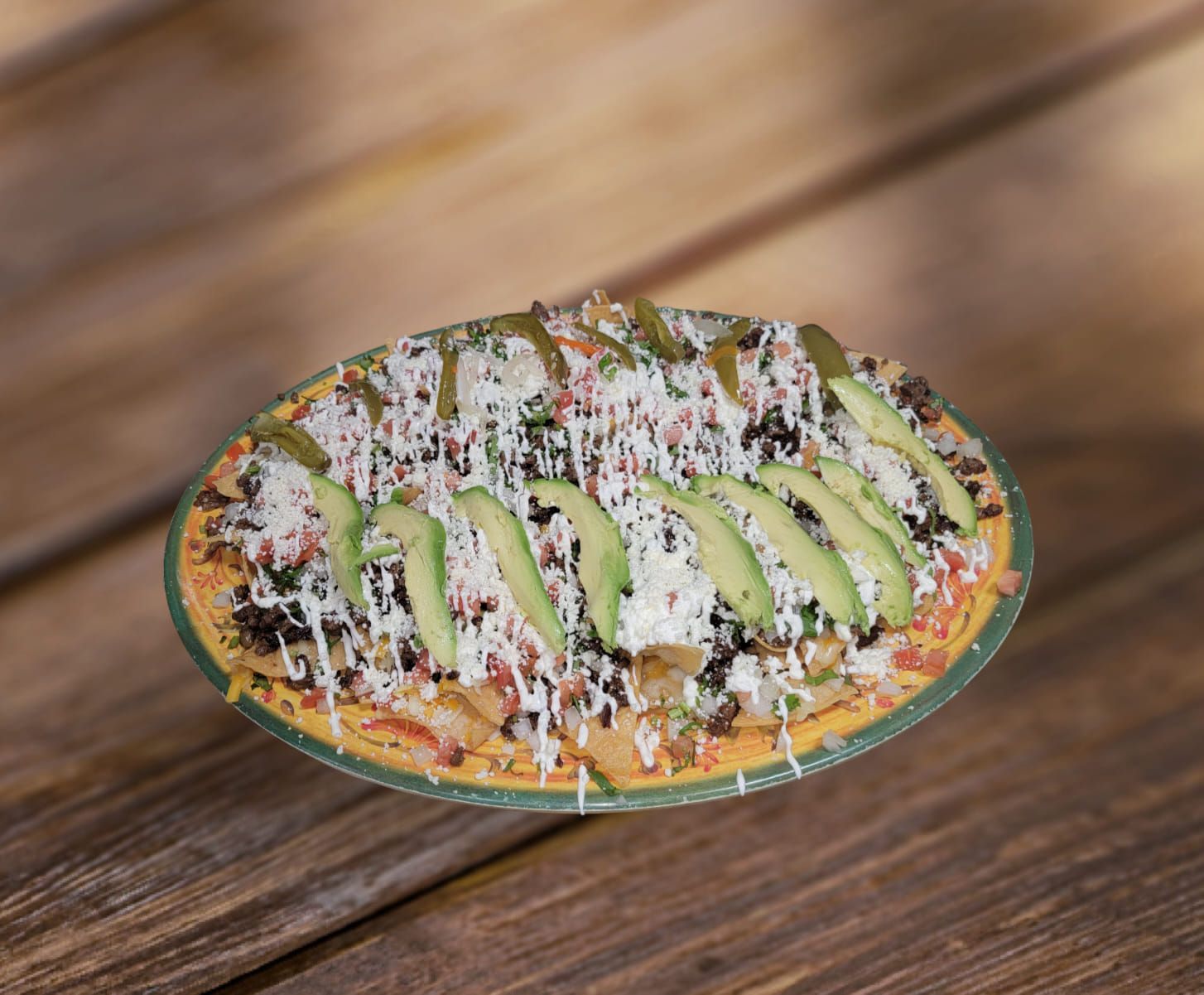 Tostada with toppings including avocado, cheese, and jalapeños on a wooden table.
