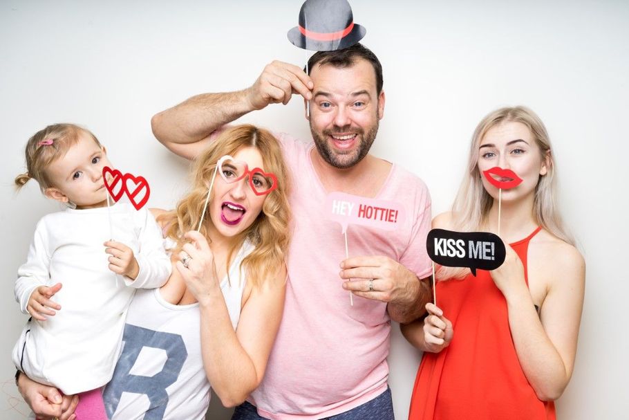 Four people posing with playful props and lips, holding a “KISS ME” sign against a white background